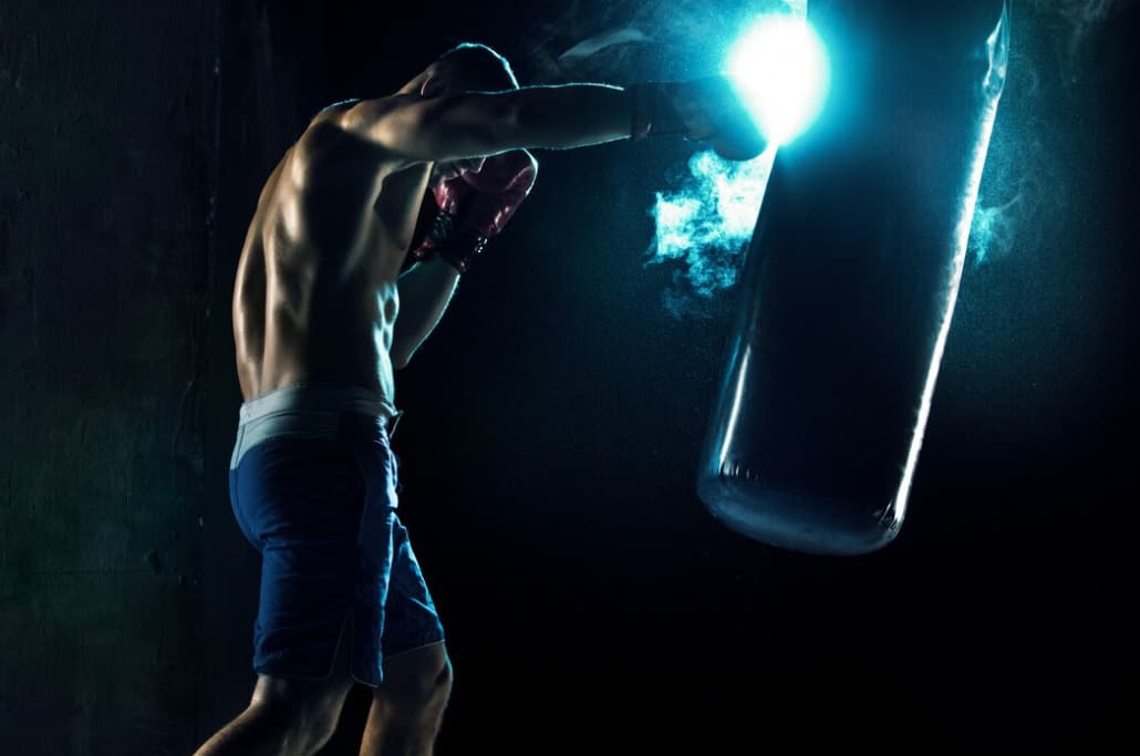 A boxer punching a heavy bag with dramatic lighting