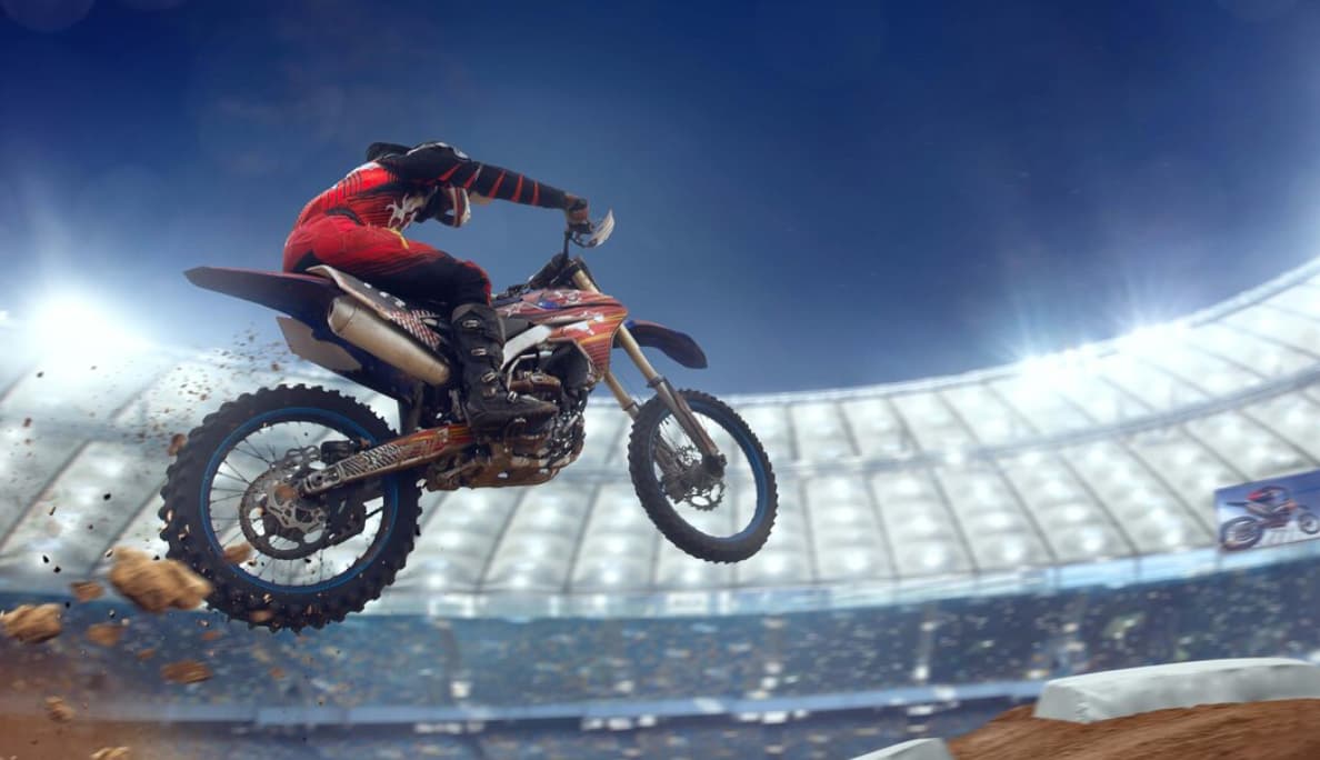 A motocross rider jumps mid-air in a stadium, dirt flying behind